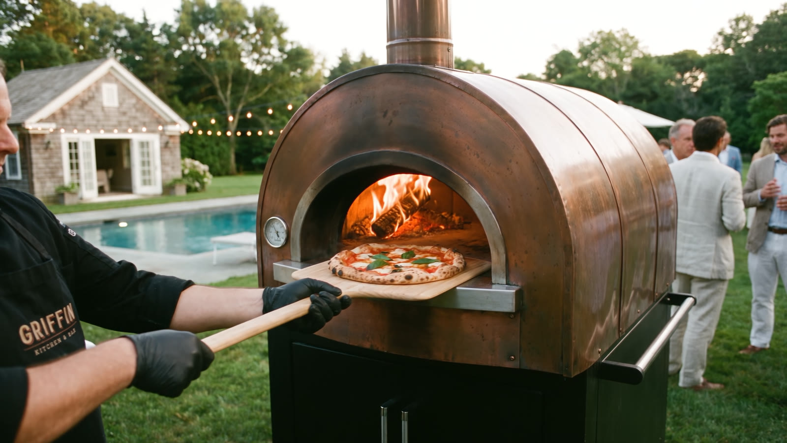 A wood-fired pizza going into a copper oven on the lawn